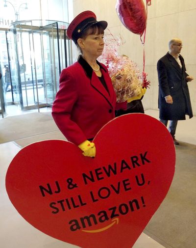 In this Feb. 14, 2019 photo provided by Newark Alliance, Laurie Ross, an actor with the event planners at Life ‘O the Party, holds the message “NJ & Newark Still Love U, Amazon!” while arriving at an Amazon office in New York. The love note came despite Amazon saying its not seeking a new site. (Associated Press)