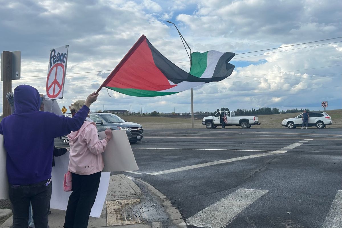 A protestor waves an Palestinian flag as Brian Bowman and Tony Rasberry counterprotest on the other side of Highway 2 just outside of Fairchild Air Force Base in Airway Heights on Saturday, April 11. (Mathew Callaghan / The Spokesman-Review)