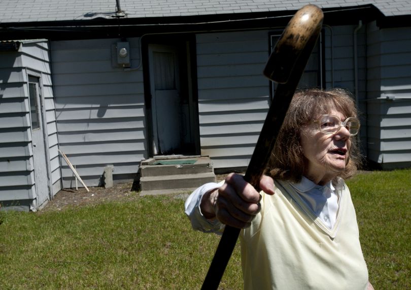 Mary Rock waves her cane Wednesday as she stands in her backyard in front of a door, center, where she says Charles Wallace entered her home in north Spokane. (Tyler Tjomsland)