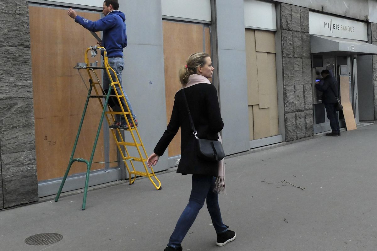 A woman walks past a worker fixing wooden pieces on a bank window near the Champs-Elysees avenue, Friday, Dec. 7, 2018 in Paris. Drastic security measures will put a lockdown on downtown Paris on Saturday as French authorities try to prevent another outbreak of violence during anti-government protests. (Bertrand Combaldieu / AP)