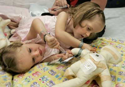 
Conjoined twins Kendra, right, and Maliyah Herrin provide medical attention to conjoined twin dolls outside their hospital room July 13 in Salt Lake City. The surgery could take 14 to 30 hours. 
 (Associated Press / The Spokesman-Review)