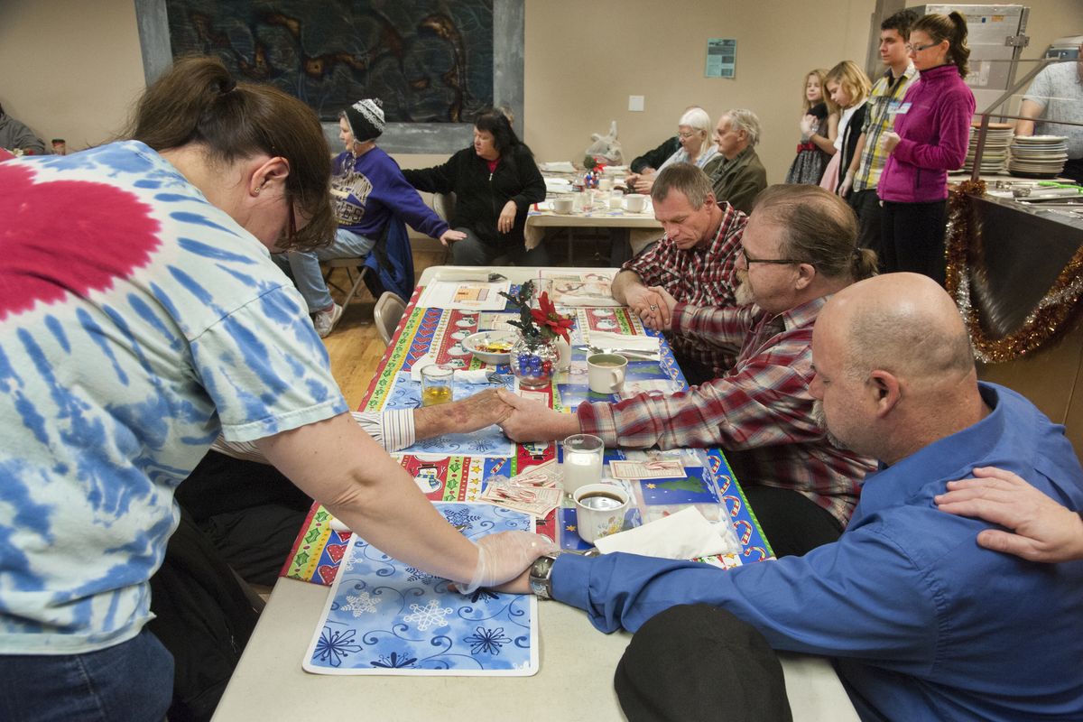 Volunteer Penny Moyer, left, joins hands for a prayer with folks gathering for the Mid-City Concerns Christmas dinner, Thursday in downtown Spokane. The Moyer family has made a tradition of giving part of their day to help at the noontime meal. (Dan Pelle)
