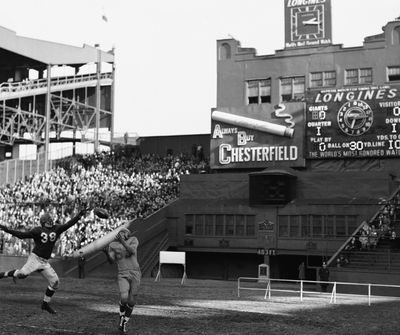 In this Nov. 14, 1948 photo, Los Angeles Rams’ Howard Hickey (53) catches a pass for a touchdown as New York Giants’ Tony Minisi (38) defends at the Polo Grounds in New York. In its early days, the NFL often relied on baseball stadiums for its teams. Often, the football team took the name of the baseball team, looking to create the illusion there was a connection between the teams. But once pro football expanded and was shown for free on television, the sport was on its way. (Associated Press)