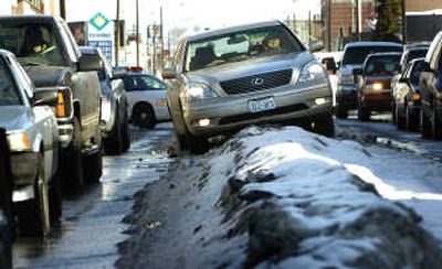 
Motorists edge past Vickie Harrington and her husband, Bill, high-centered on a Second Avenue snow berm in Spokane on Thursday.  Harrington said she was temporarily blinded by the sun reflecting off the wet road and found herself atop the snow. Spokane police warn that trying to drive over berms can result in damage or embarrassment. 
 (Rajah Bose / The Spokesman-Review)