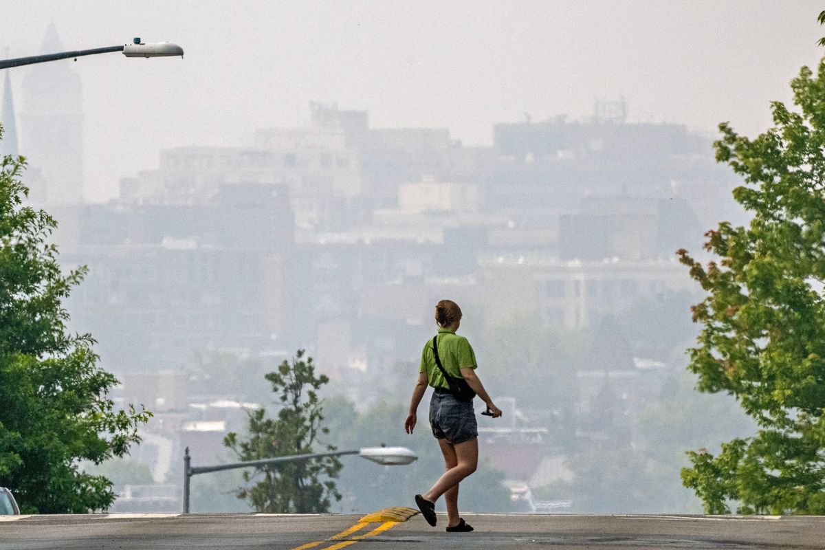 A woman crosses a street as smoke from the Canadian wildfires renders the cityscape amorphous in Washington, D.C.  (Bill O