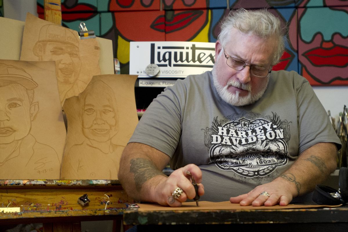 Sam White works on a leather portrait on Wednesday, in front of leather portraits of his grandchildren, at his home studio in Spokane. White is a plumber, a Harley-Davidson enthusiast and an artist. (Tyler Tjomsland)