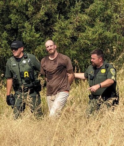 Cory James Magruder is led Tuesday by two law enforcement officials through a field south of Davenport. Magruder reportedly escaped from the Lincoln County Jail in Davenport Monday night and was captured Tuesday.  (Courtesy of Lincoln County Sheriff's Office)