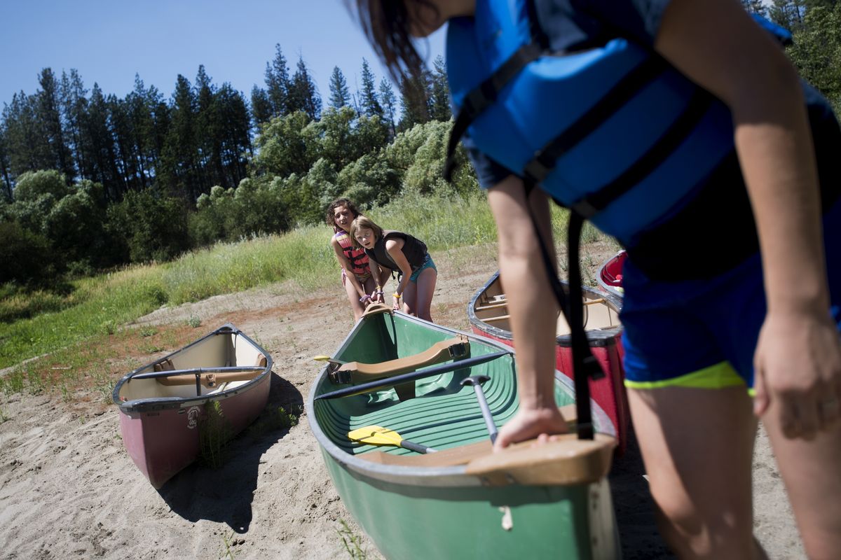 Camp counselor Kristiana Arellanes leads Kaydence Johnson, 9, left, and Samantha Hawker, 9, in pushing a canoe into the river at Union Gospel Mission’s summer camp in Ford, Wash., on Thursday. (Tyler Tjomsland)