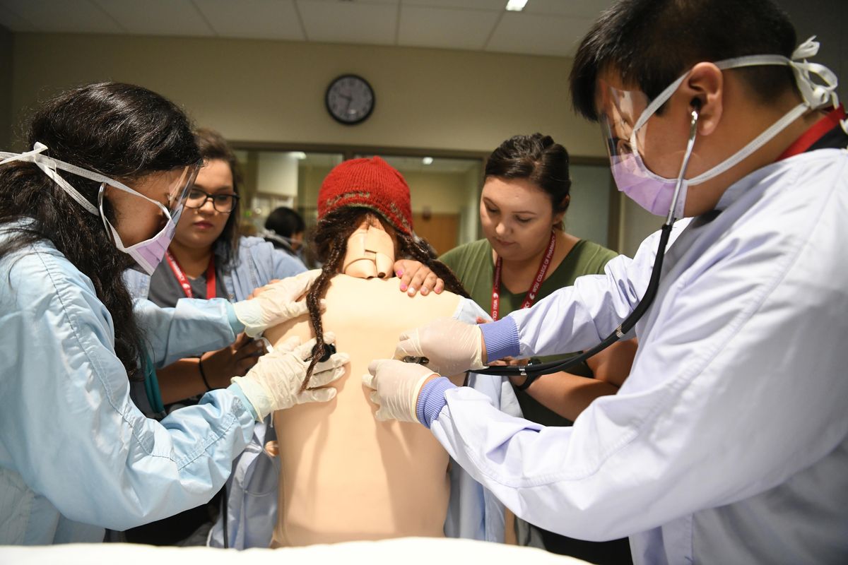 Roland Weaskus, left, and Ryan Hill, right, use stethoscopes to listen to the chest of a medical mannequin with the help of nursing students Terrin Utter, center left, and Sarah Burke, center right, in the nursing simulation lab at the Washington State University Nursing School in Spokane, Tuesday, June 19, 2018. Weaskus and Hill are Native American youth with an interest in medical professions who were in the WSU nursing simulation lab to get a taste of possible professions. (Jesse Tinsley / The Spokesman-Review)
