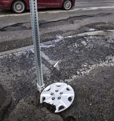 A broken hubcap sits alongside broken pavement at the corner of Freya Street and Congress Avenue, Feb. 17, 2017, in Spokane, Wash. (Dan Pelle / The Spokesman-Review)