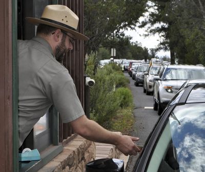 Nate Powell, an employee with Grand Canyon National Park, collects an entrance fee as traffic is backed up as vehicles arrive Aug. 2, 2015, at an entrance gate at Grand Canyon National Park, Arizona. A new study concludes visitors may be steering clear of some U.S. national parks or cutting their visits short because of pollution. (Emery Cowan / AP)