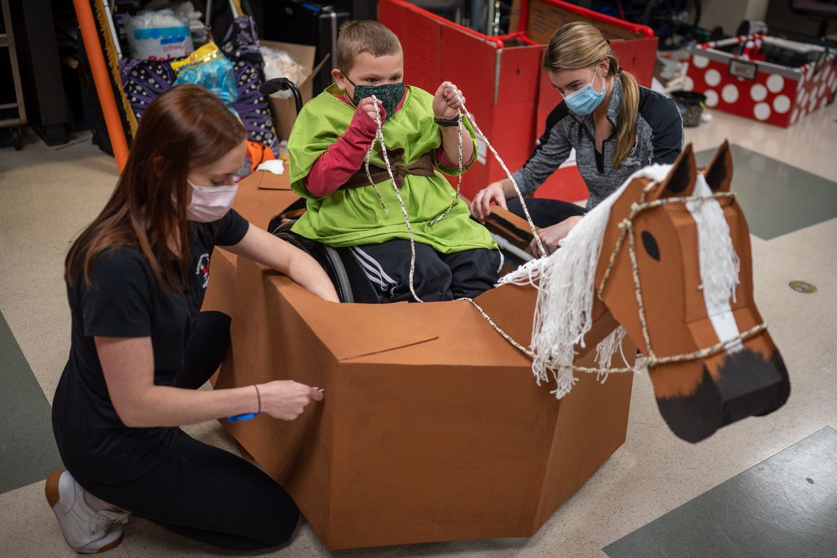 EWU occupational therapy student Kendra Clark, left, and EWU physical therapy student Kaitlyn Detlefsen assemble a cardboard medieval horse Thursday around the wheelchair of Emmett Sonnemaker, 6. Shriners Hospital for Children in Spokane has partnered with EWU occupational and physical therapy students to create wheelchair-adaptable costumes for Halloween.  (Colin Mulvany/The Spokesman-Review)