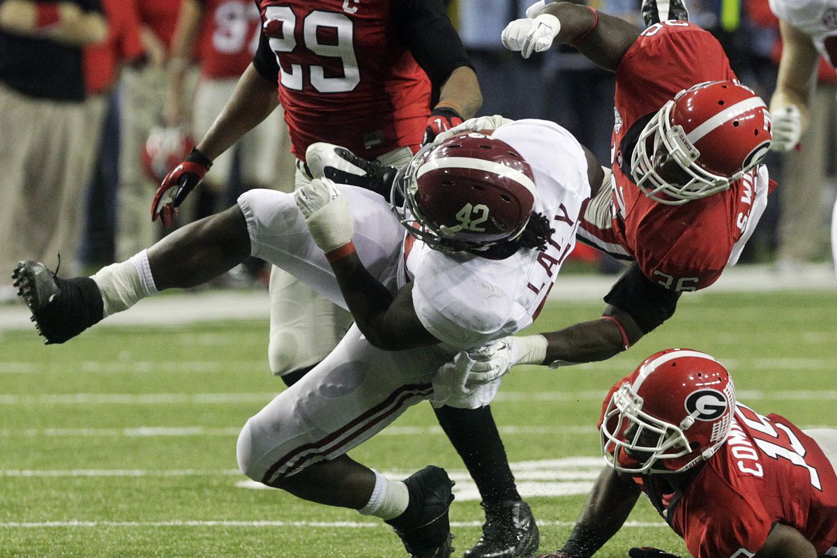 Georgia’s Shawn Williams takes to the air to tackle Alabama running back Eddie Lacy as Sanders Commings, bottom, looks on. (Associated Press)