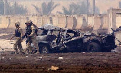 
American soldiers walk past a vehicle damaged in a car bomb explosion at Baghdad International Airport.
 (Associated Press / The Spokesman-Review)