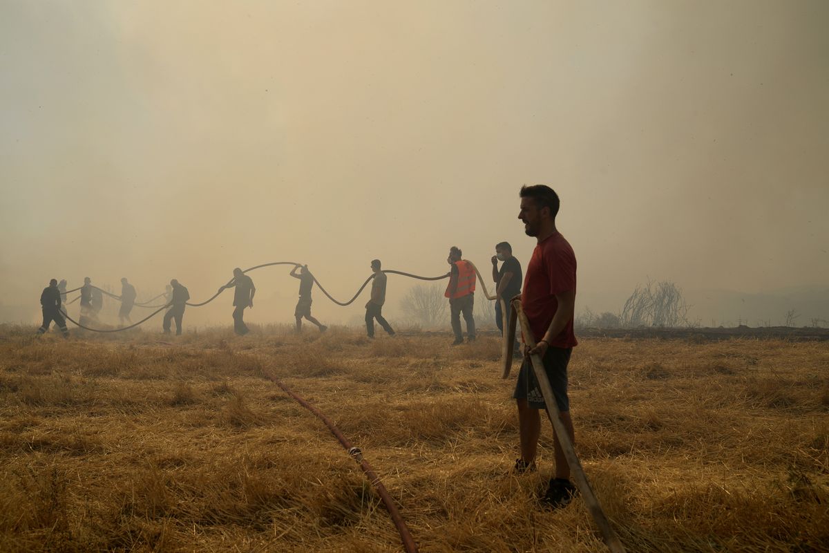 A firefighter tries to extinguish a fire as volunteers hold the water hose in Agios Stefanos, in northern Athens, Greece, Friday, Aug. 6, 2021. Thousands of people have fled wildfires burning out of control in Greece and Turkey, including a major blaze just north of the Greek capital of Athens that left one person dead.  (Thanassis Stavrakis)