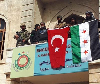 A Turkish and a Turkey-backed Free Syrian Army soldier wave Turkish and FSA flags in the city center of Afrin, northwestern Syria, early Sunday, March 18, 2018. (Hasan Kirmizitas / Associated Press)