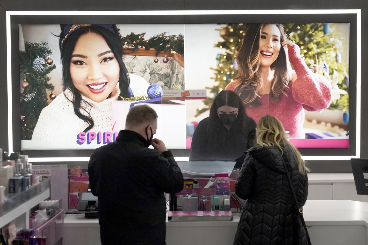Cashier Druhan Parker, center, works behind a plexiglass shield Thursday, Nov. 19, 2020, as he checks out shoppers at an Ulta beauty store on Chicago