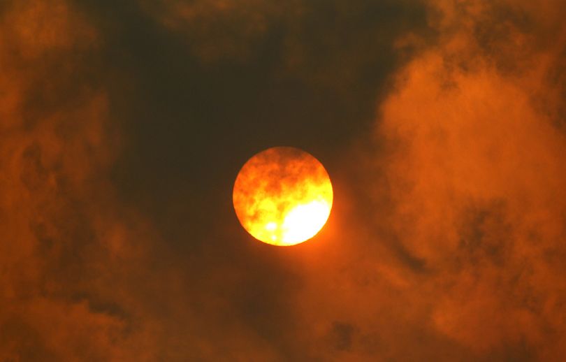 The sun and nearby clouds of smoke turn a brilliant red where a wildfire burns past the paved section of Number 1 Canyon Road Monday, Sept. 10, 2012, near Wenatchee, Wash. Crews in central Washington and Wyoming worked Monday to protect homes from two of the many wildfires burning throughout the West as a destructive fire season stretches into September with no relief expected from the weather anytime soon. The National Weather service issued red-flag warnings for wide swaths of eastern Washington and Oregon, Idaho, Montana and all of Wyoming, meaning conditions could exacerbate blazes. (Elaine Thompson / Associated Press)