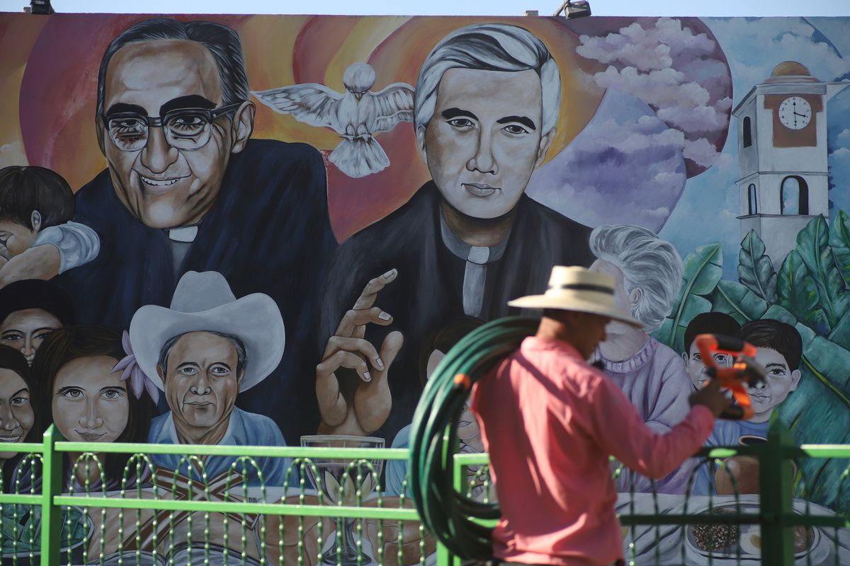 A gardener puts away his tools as he wraps up for the day backdropped by a mural featuring the late Archbishop Oscar Romero and Rev. Rutilio Grande in the Plaza de Los Martires or Martyrs Square, Friday in El Paisnal, El Salvador.  (Salvador Melendez)