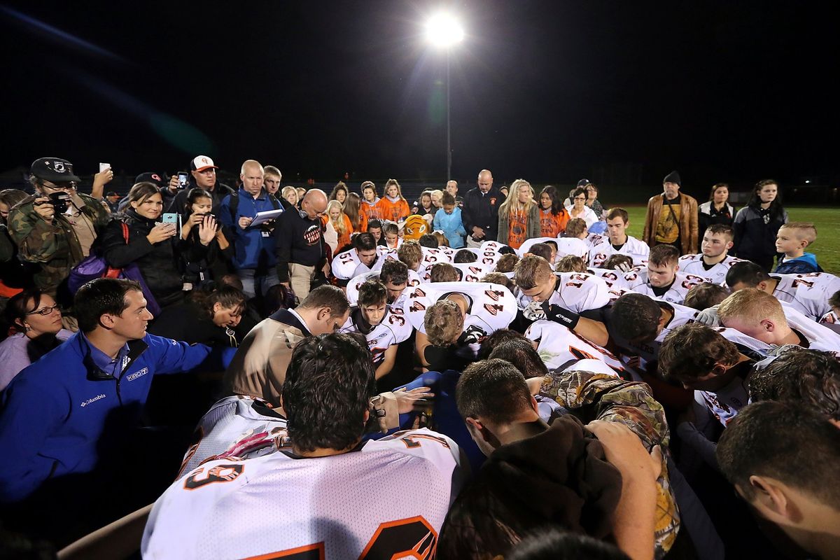 FILE - Bremerton assistant football coach Joe Kennedy, obscured at center in blue, is surrounded by Centralia High School football players as they kneel and pray with him on the field after their game against Bremerton on Oct. 16, 2015, in Bremerton, Wash. After losing his coaching job for refusing to stop kneeling in prayer with players and spectators on the field immediately after football games, Kennedy will take his arguments before the U.S. Supreme Court on Monday, April 25, 2022, saying the Bremerton School District violated his First Amendment rights by refusing to let him continue praying at midfield after games.  (Meegan M. Reid)