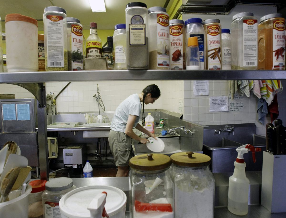 Keri Rainsberger cleans dinner dishes for members of her “intentional community” at the Keystone Ecological Urban Center in Chicago.  Although Rainsberger earns a low salary, her shared living arrangement frees her of the economical squeeze other Americans are feeling. (The Spokesman-Review)
