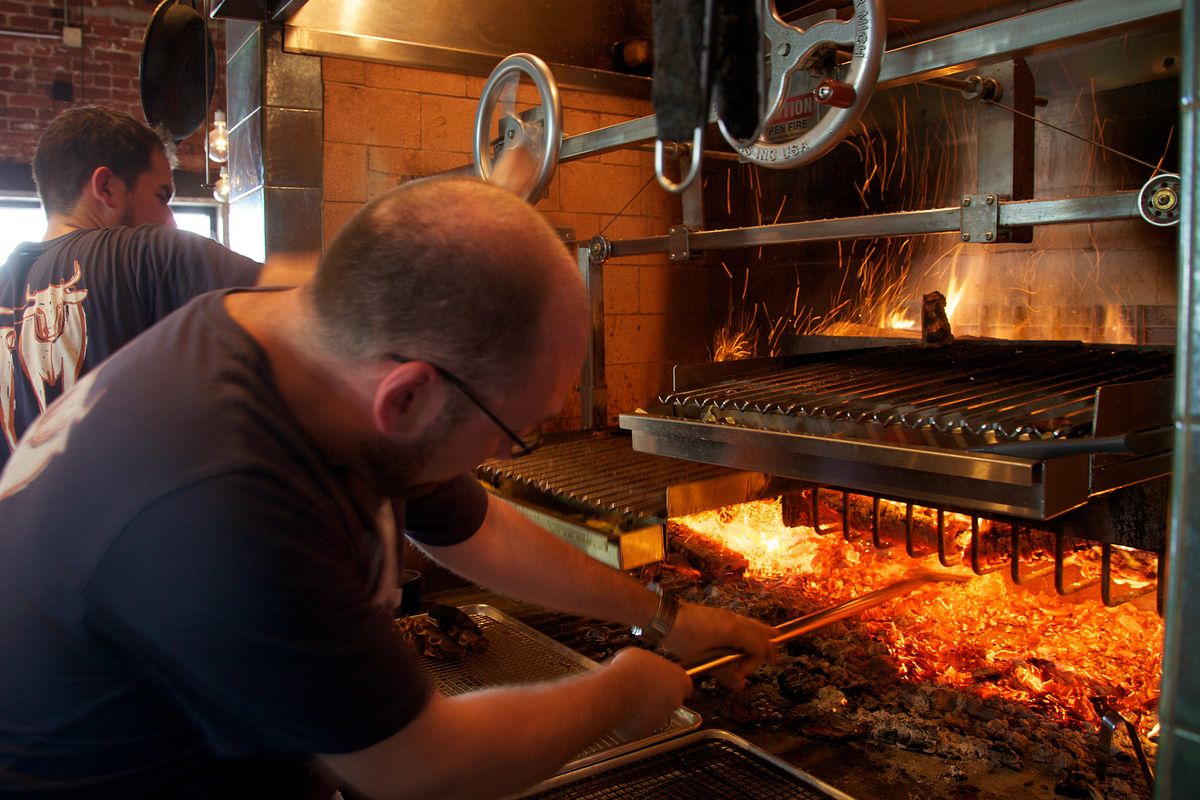 Owner and chef Greg Denton checks the fire of the grill at Ox in Portland. (Associated Press)