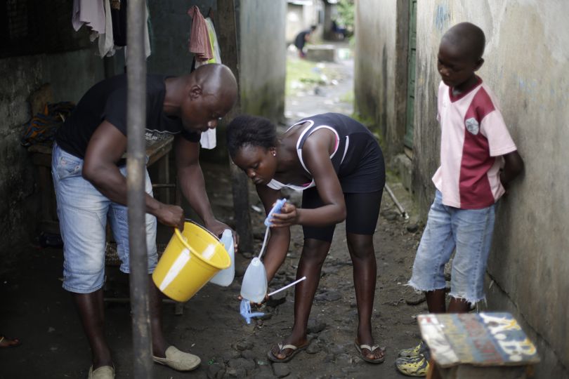 In this photo taken Thursday Oct. 2, 2014, Promise Cooper, 16,  is helped filling a bottle with  chlorine solution by  Kanyean Molton Farley, a community activist who visits Promise and her two brothers, Emmanuel Junior, 11, right,  and Benson, 15, not pictured,  on a daily basis at their St. Paul Bridge home in Monrovia, Liberia. The Cooper children are now orphans, having lost their mother, Princess, in July, and their father Emmanuel in August. Their 5-month-old baby brother Success also succumbed to the virus in August. Ruth, their 13-year-old sister is being hospitalized with Ebola. The three never fell sick to the deadly disease. (Jerome Delay / Associated Press)