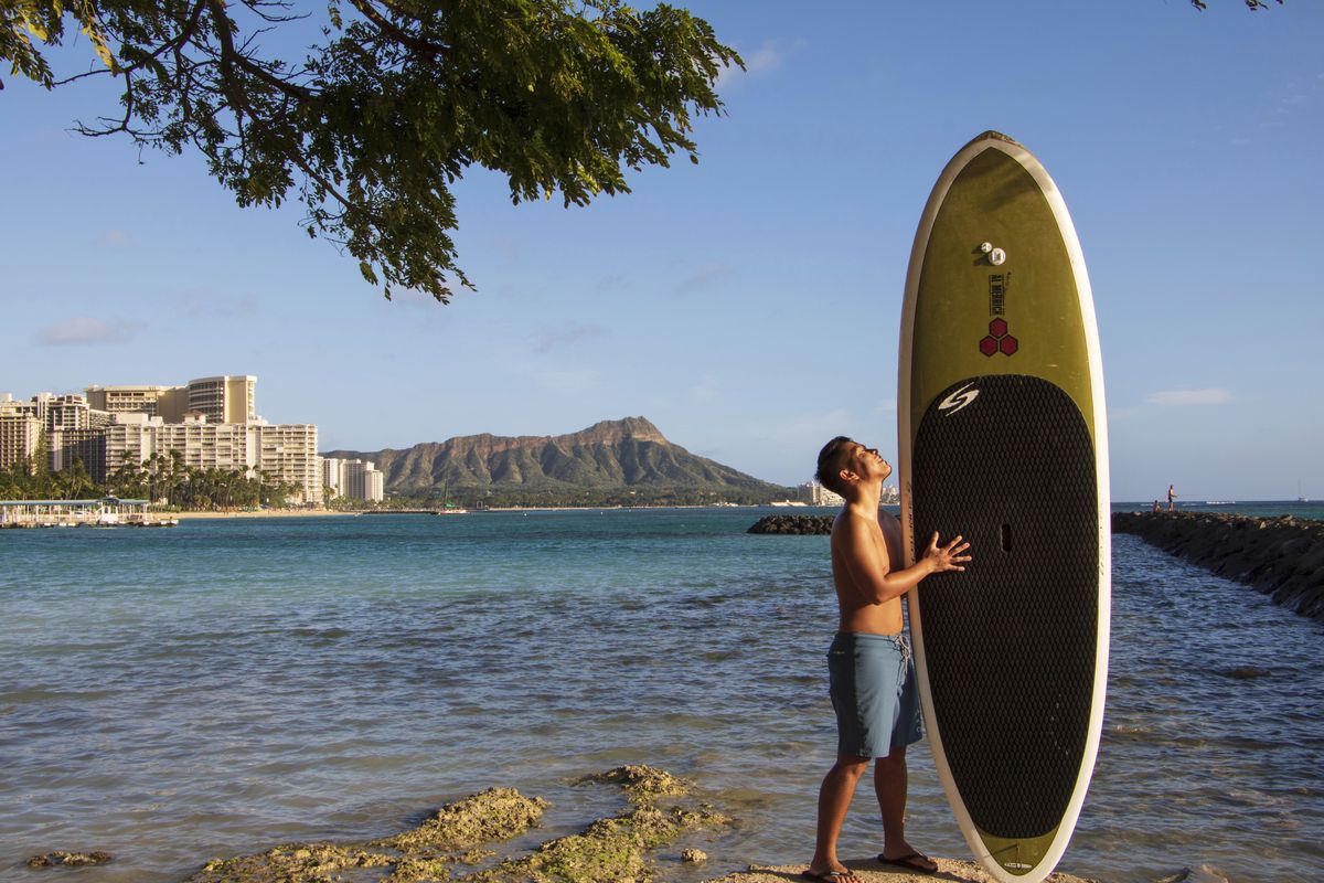 In this photo provided by Yoko Liriano, Bryant de Venecia poses for a photo with his paddleboard in Honolulu, Wednesday, Nov. 11, 2020. He started stand-up paddle-boarding when there were fewer tourists coming to Hawaii during the pandemic. He