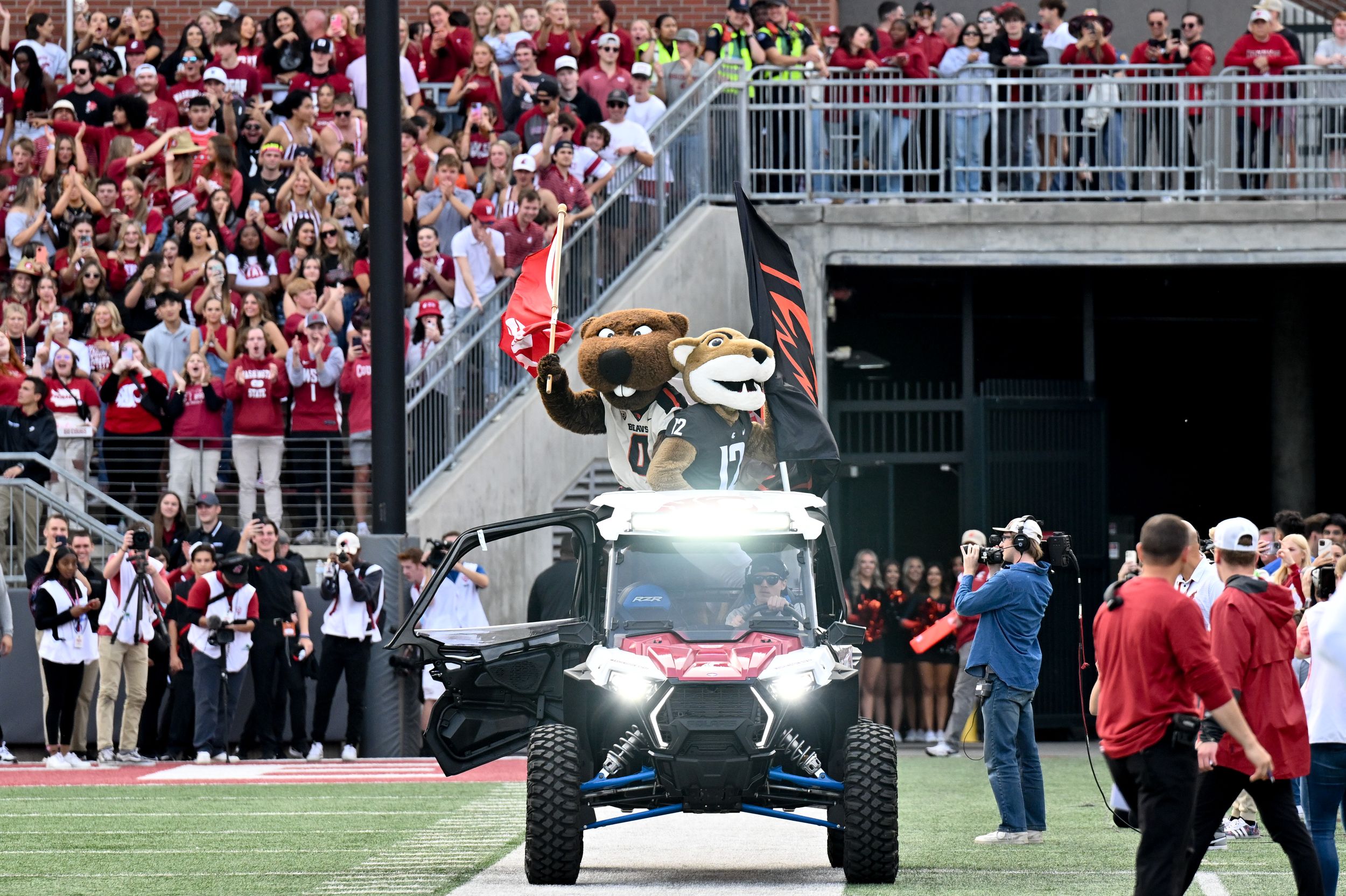 Cougar and Beaver mascots carry flags on the back of a 4x4 in the Cougars football stadium