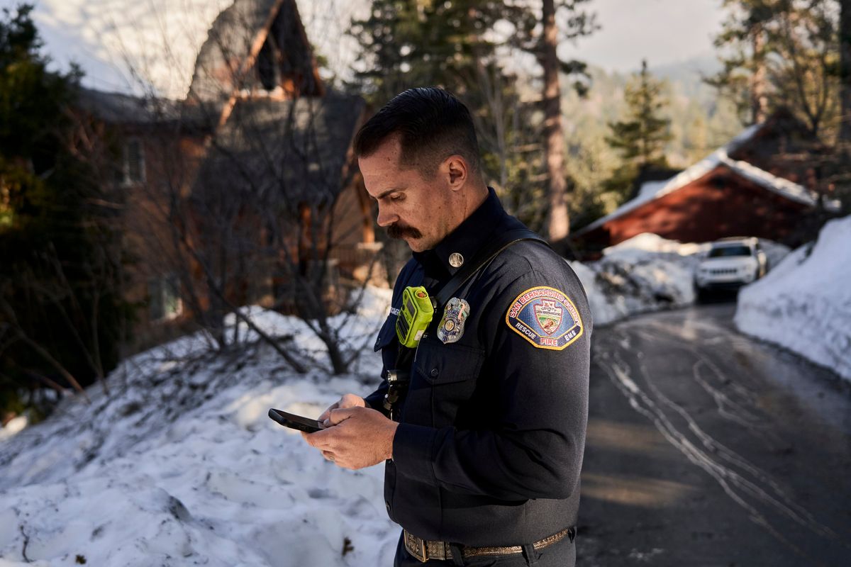 Capt. Jared Newcomer of the San Bernardino County Fire Department uses his cellphone while visiting a residential neighborhood in Twin Peaks, Calif., on Monday.  (Philip Cheung/For The Washington Post)