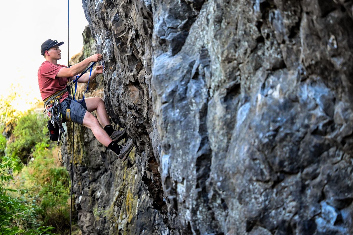 Zach Turner with the Bower Climbing Coalition replaces quick draws and climbing bolts on a basalt rock crag below Cliff Drive, Wednesday, July 27, 2022. A group of climbers with the coalition spent the afternoon removing graffiti, picking up trash and replacing anchors on the rock faces.  (COLIN MULVANY/THE SPOKESMAN-REVIEW)