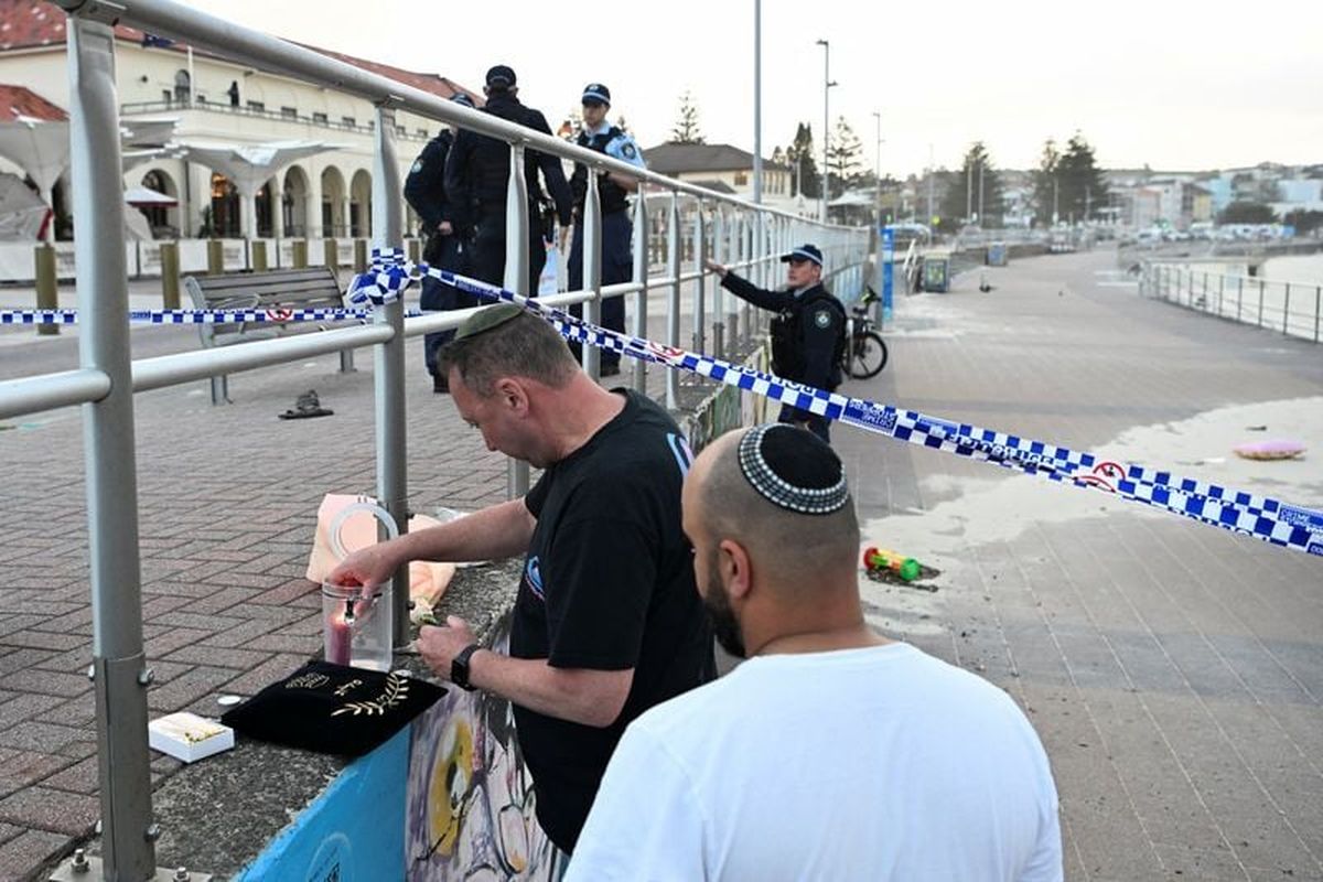 A man lights a candle as police officers stand guard following the attack on a Jewish holiday celebration on Sunday at Sydney