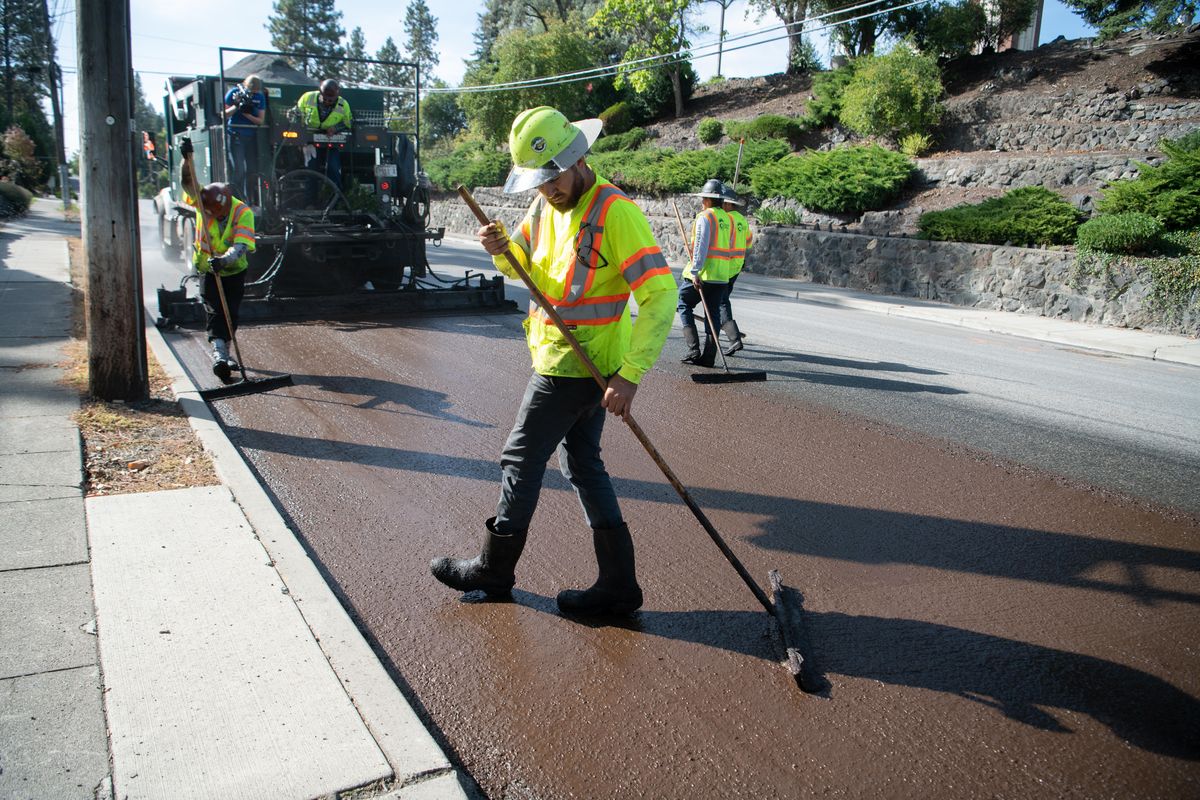 Workers use squeegees to smear the slurry sealant being laid down by the truck owned by Intermountain Slurry Seal on Bernard Street in Spokane Saturday, Sept. 21, 2019. The sealing method is new to Spokane. (Jesse Tinsley / The Spokesman-Review)
