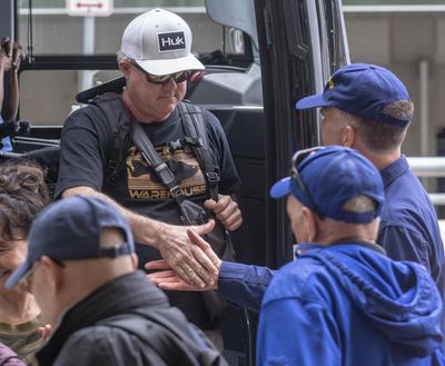 A man in a white hat shakes hands with people at San Antonio International Airport Tuesday, March 3, 2020 as he gets off a bus that arrived from JBSA-Lackland. (William Luther / associated press)