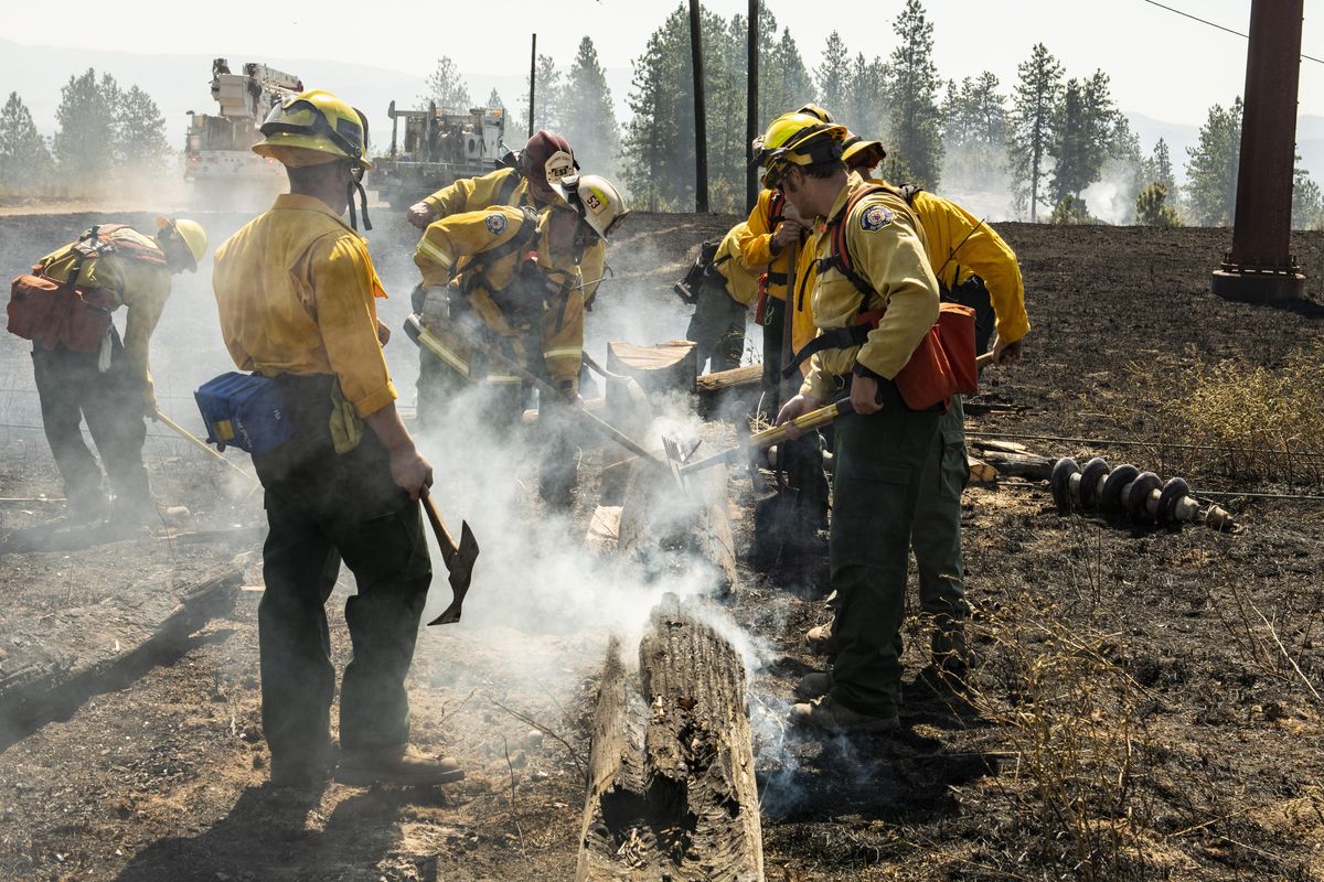 After an Avista crew cut down the remnants of a charred power pole along East Valley Springs Road, Firefighters from Snohomish County dig out the burning parts as they do mop up work on Wednesday, July 18, 2018. Firefighters have built a line completely around the fire that destroyed a home and burned 115 acres, Tuesday along Upriver Drive near Camp Sekani . (Colin Mulvany / The Spokesman-Review)