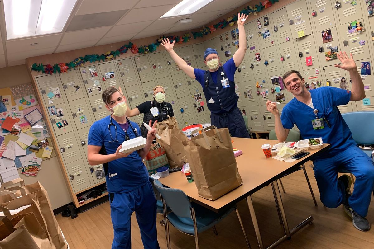 Oregon Health & Science University nurses, from left, Nick Greenwood, Callie Harling, Derrell Wheeler and Orion Meredith gesture as they eat a meal delivered on Jan. 10 to the hospital’s frontline COVID-19 health care workers in a break room at Oregon Health & Science University in Portland.  (Brittney Caldera)