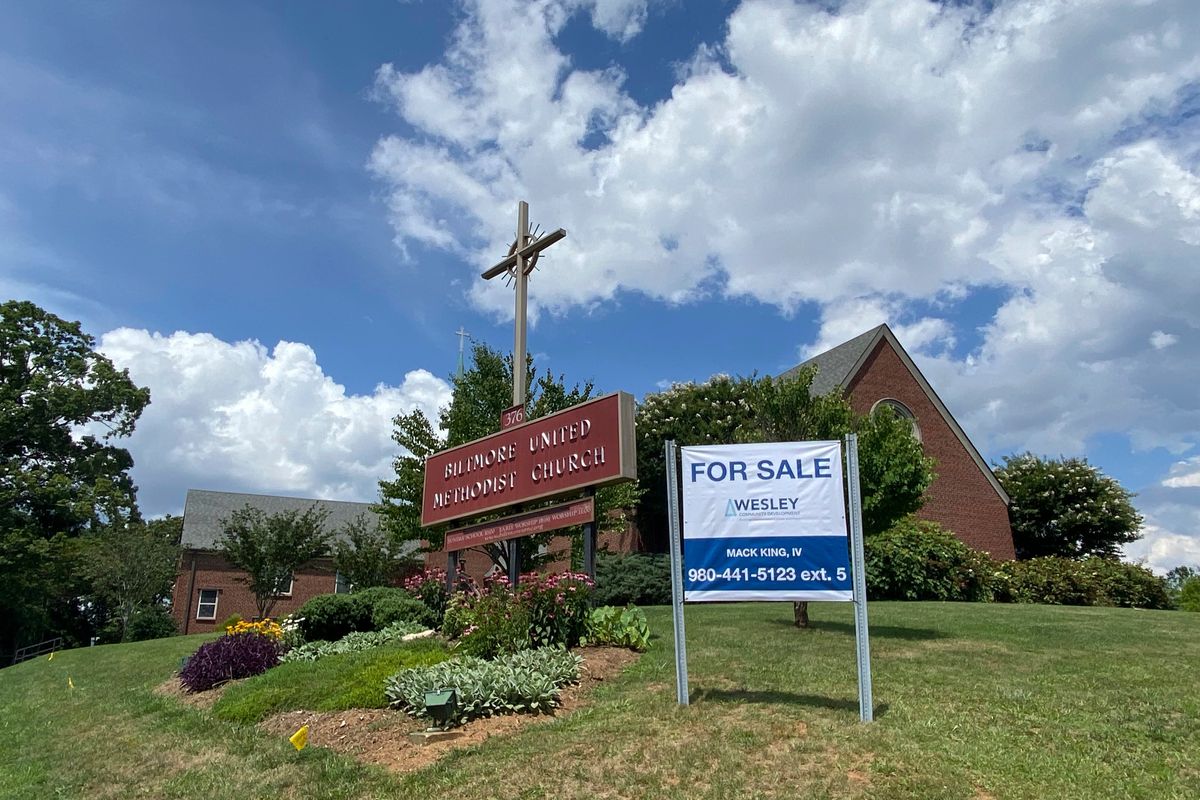 This photo provided by the Rev. Lucy Robbins shows a "For Sale" sign in front of the Biltmore United Methodist Church in Asheville, N.C. in July 2021. Already financially strapped because of shrinking membership and a struggling preschool, the congregation was dealt a crushing blow by the coronavirus. Attendance plummeted, with many staying home or switching to other churches that stayed open the whole time. Gone, too, is the revenue the church formerly got from renting its space for events and meetings.  (Lucy Robbins)