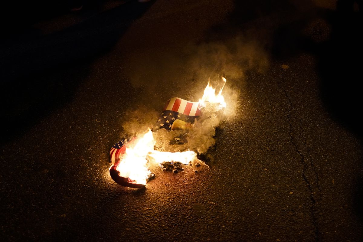 In this Nov. 14, 2020 photo, a sign that counter-protesters lit on fire burns after supporters of President Donald Trump held pro-Trump marches Saturday, in Washington. Reports of hateful and violent speech on Facebook poured in on the night of May 28 after President Donald Trump hit send on a social media post warning that looters who joined protests following Floyd