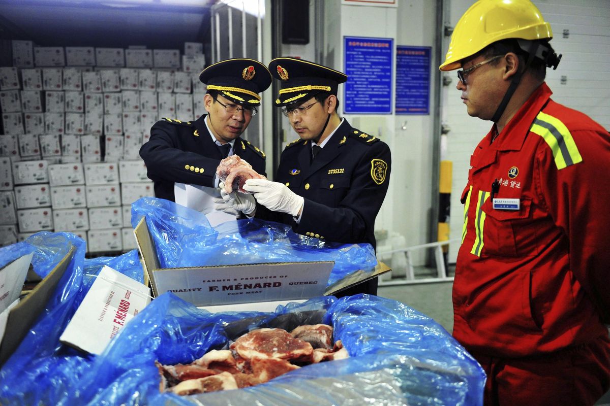 In this April 13, 2017, photo, a warehouse worker watches as government inspectors check imported frozen pork in Qingdao in eastern China’s Shandong province. China announced a list of U.S. goods including pork, apples and steel pipe on Friday, March 23, 2018, that it said may be hit with higher import duties in response to President Donald Trump’s tariff hike on steel and aluminum. (Associated Press)