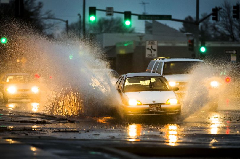 An evening commuter hits a large street puddle at the intersection of Indiana Avenue and Atlanta Street after rainfall set a daily record  on Dec. 7, 2015, in Spokane, Wash. The recent windstorm left many storm drains clogged with debris, which caused widespread street flooding around town. (Colin Mulvany / The Spokesman-Review)