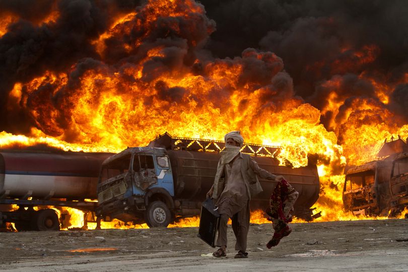 An Afghan carries his belongings as he passes burning fuel tankers in the outskirts of Kabul, Afghanistan, Thursday, Aug. 4, 2011. Police said around five fuel tankers carrying fuel for NATO and U.S. forces in Afghanistan caught fire inside a depot in Kabul. No casualties were reported, and it was not immediately clear what caused the fire. (Dar Yasin / Associated Press)