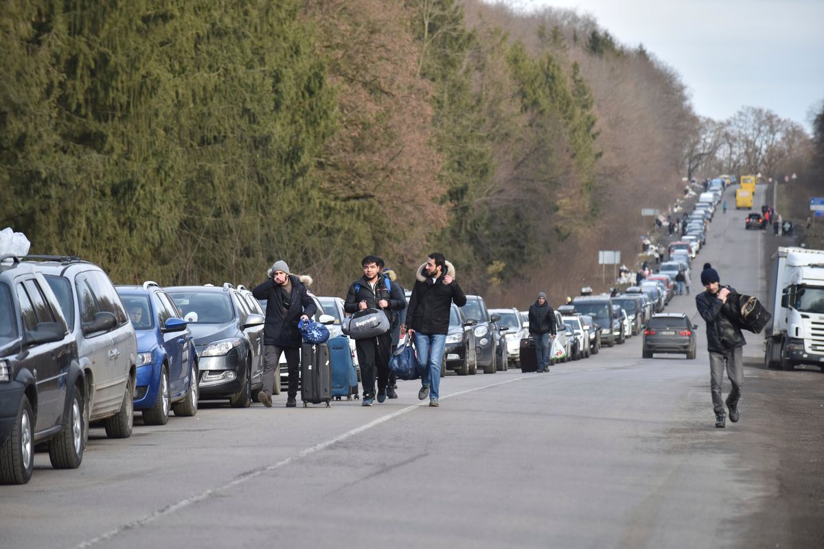 People walk past a queue of cars heading to the Poland border Tuesday near Shehyni, western Ukraine. Russian shelling pounded civilian targets in Ukraine’s second-largest city again, and a 40-mile convoy of tanks and other vehicles threatened the capital.  (Pavlo Palamarchuk)