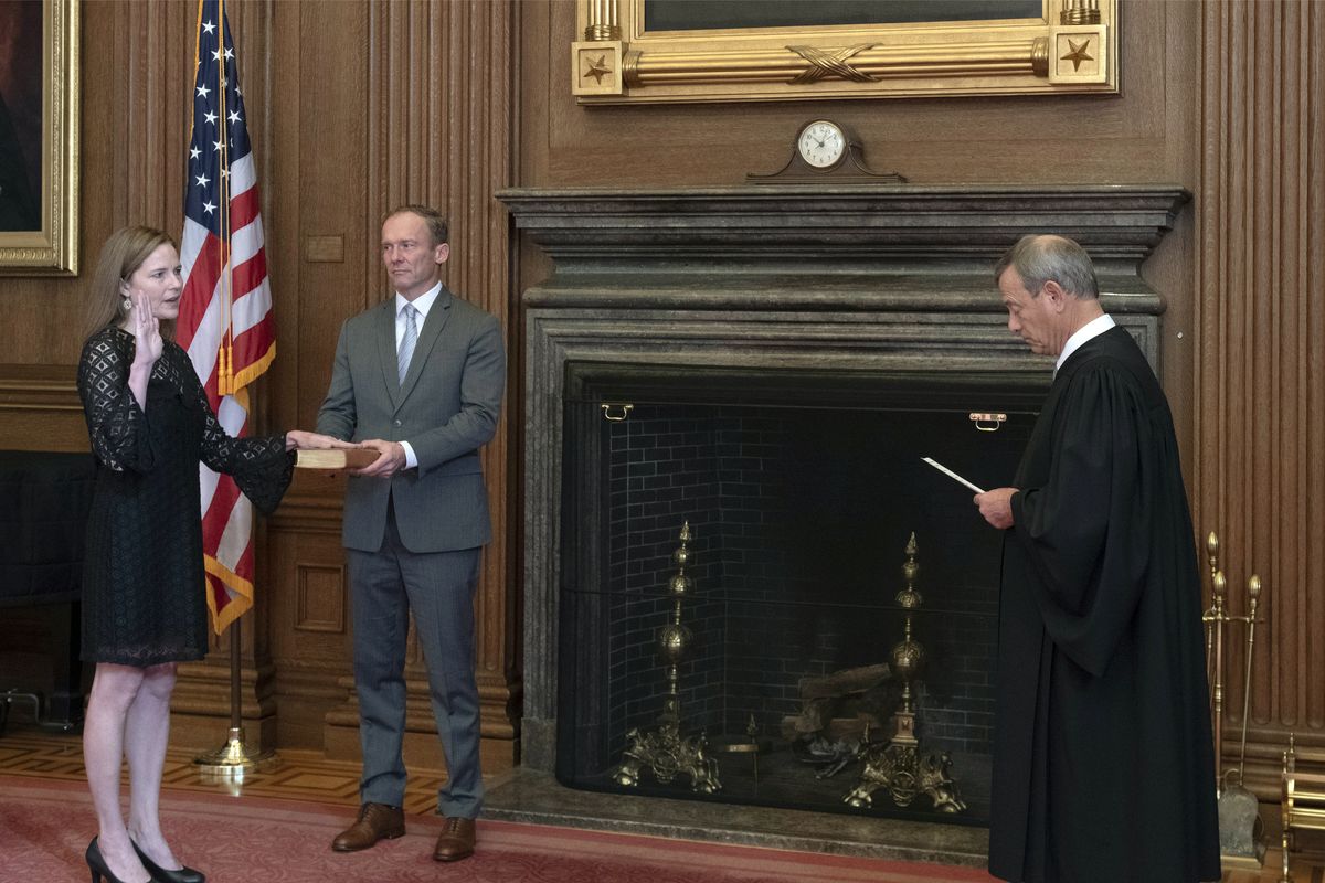In this image provided by the Collection of the Supreme Court of the United States, Chief Justice John G. Roberts, Jr., right, administers the Judicial Oath to Judge Amy Coney Barrett in the East Conference Room of the Supreme Court Building, Tuesday, Oct. 27, 2020, in Washington as Judge Barrett’s husband, Jesse M. Barrett, holds the Bible.  (Fred Schilling)