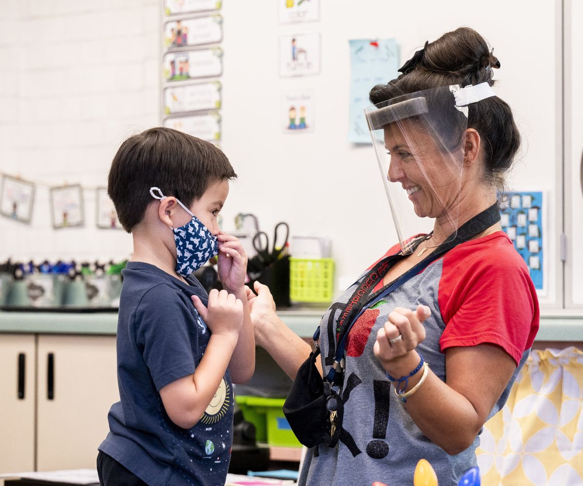 In this Aug. 12, 2021 photo, a student gets help with his mask from transitional kindergarten teacher Annette Cuccarese during the first day of classes at Tustin Ranch Elementary School in Tustin, Calif. Now that California schools have welcomed students back to in-person learning, they face a new challenge: A shortage of teachers and all other staff, the likes of which some districts say they