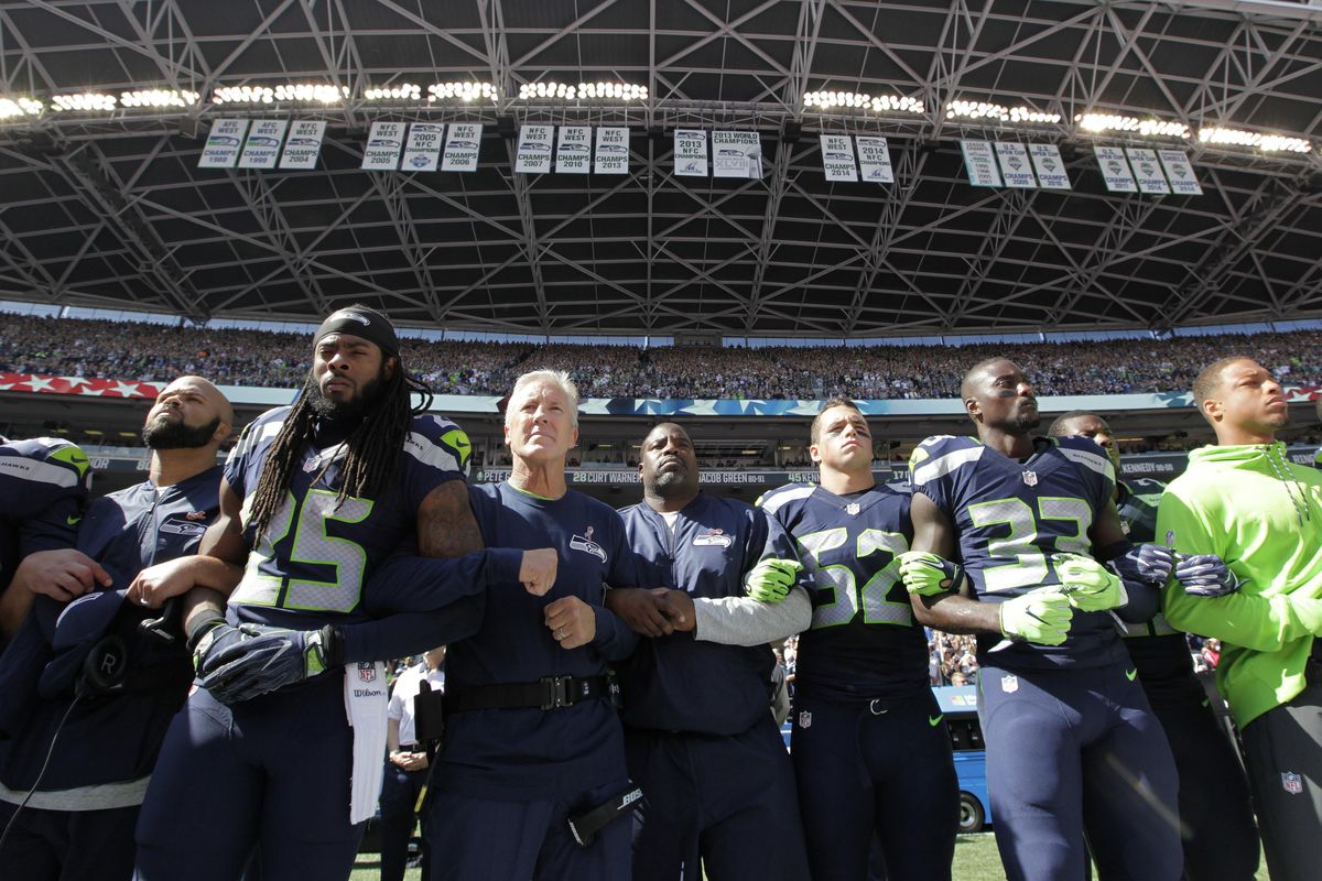 Seahawks players and coaches, including cornerback Richard Sherman (25) and head coach Pete Carroll, third from left, stand and link arms Sunday during the singing of the national anthem before an NFL football game against the Miami Dolphins. (Elaine Thompson / Associated Press)