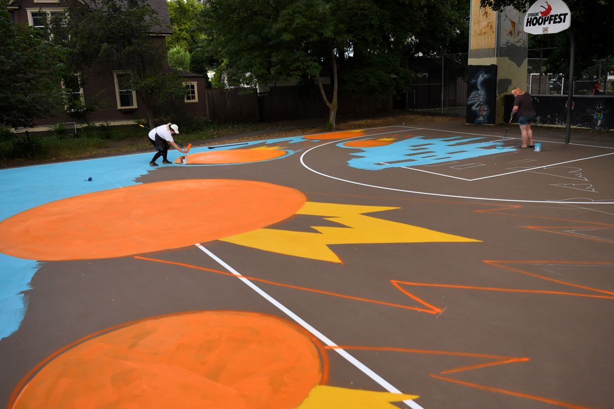 Artist Tiffany Patterson, right, and her assistant Bella Campos, left, work to paint a Hooptown mural on the Peaceful Valley Park basketball court on Tuesday, July 14, 2020, in Spokane, Wash.  (Tyler Tjomsland/The Spokesman-Review)