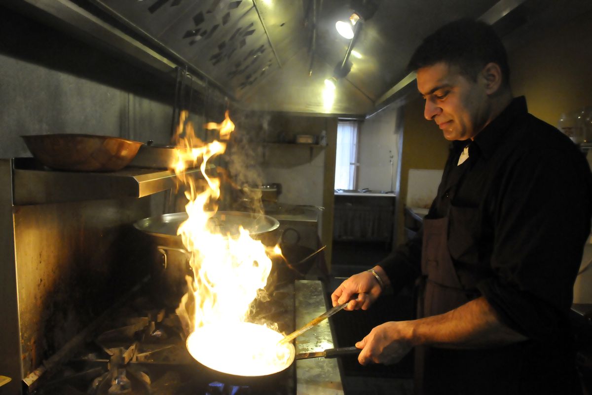 A cook in a Sikh kitchen cooking in an extremely large pot.