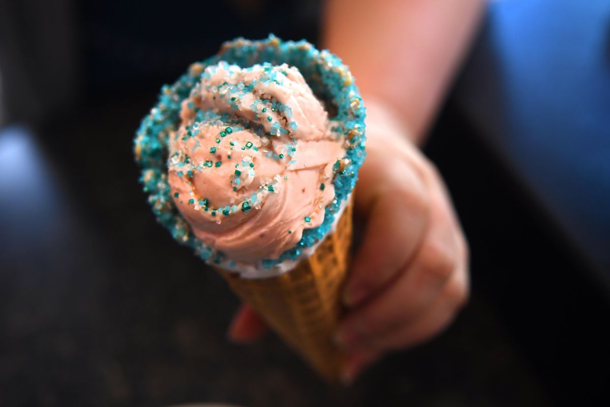 The Scoop ice cream shop owner Jennifer Davis holds "Crystal" the prickly pear lemonade ice cream with sprinkles at the shop on Wednesday, April 25, 2018. They named the cone after the main character in Cirque du Soleil on honor of their visit to Spokane. (Kathy Plonka / The Spokesman-Review)
