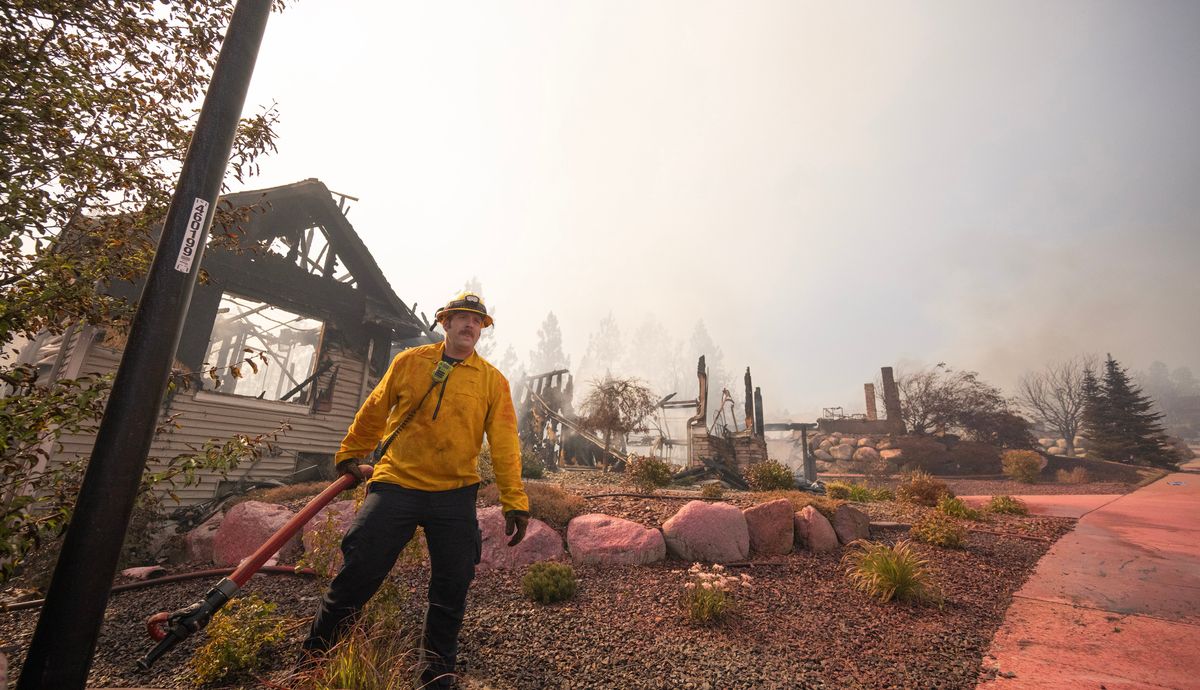 A Spokane firefighter pulls a hose away from a destroyed home on Emerald Lane in Spokane Valley on June 16, 2026, after a wildfire swept through the neighborhood.  (Brian Plonka/The Spokesman-Review)