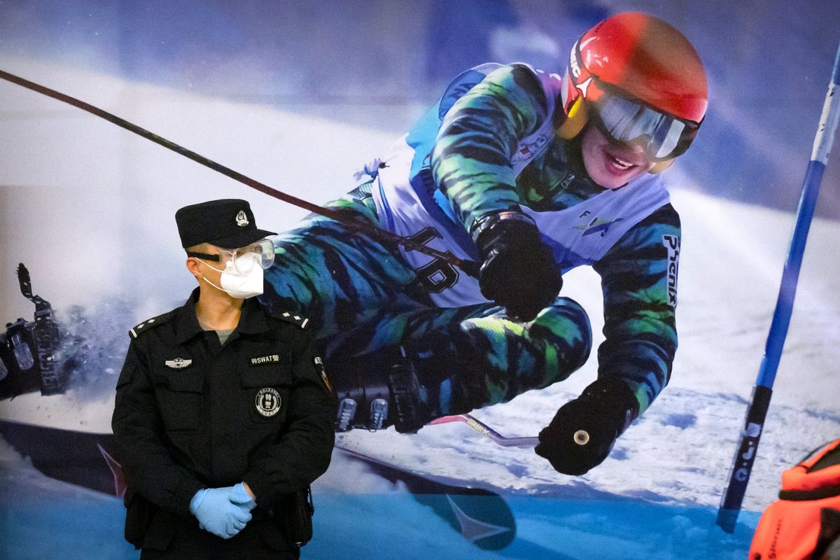 FILE - A police officer wearing a face mask and goggles to protect against COVID-19, stands near a poster of a skier on the wall at a train station in Zhangjiakou in northern China